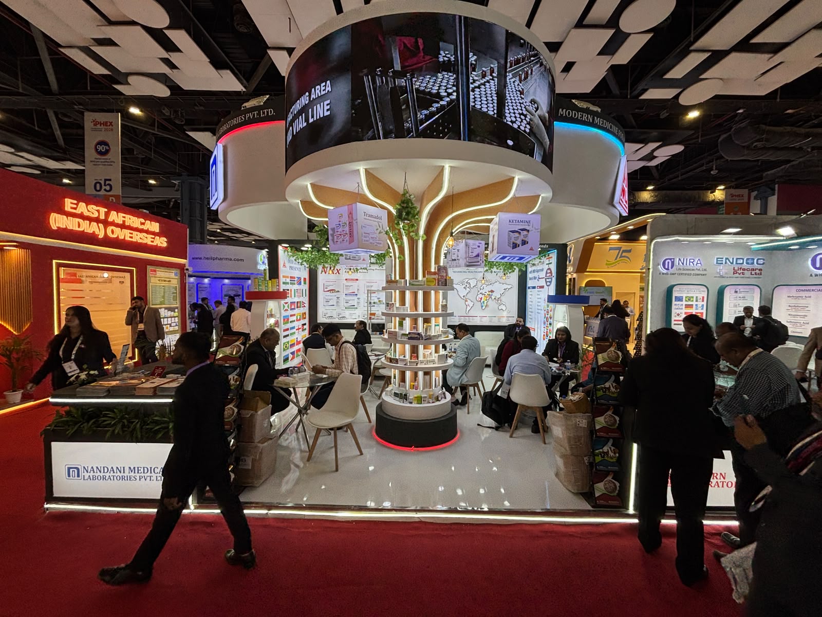 Nandani stall from the aisle — central tree column with hanging product boxes and circular shelves beside the neighbouring red booth