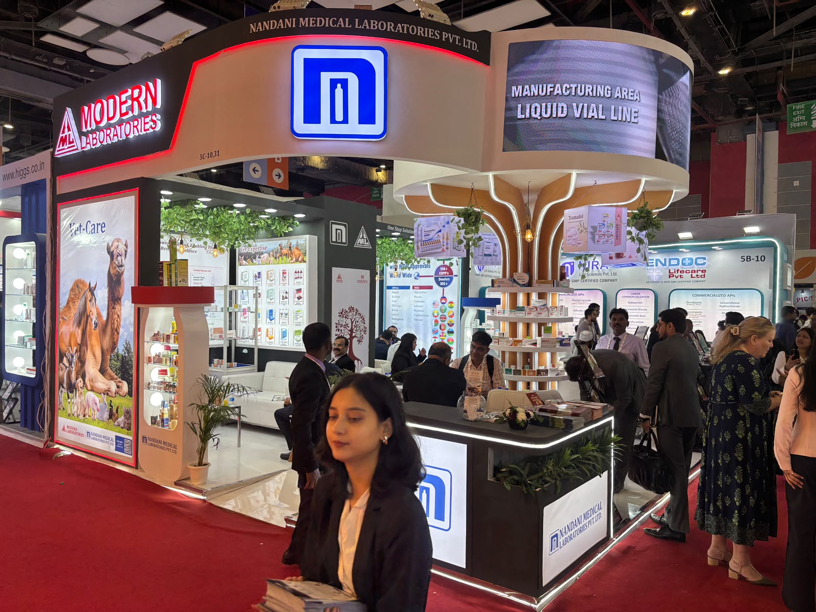 Nandani stall left elevation — Modern Laboratories fascia, blue backlit ML monogram, LIQUID VIAL LINE screen and Vet-Care animal poster