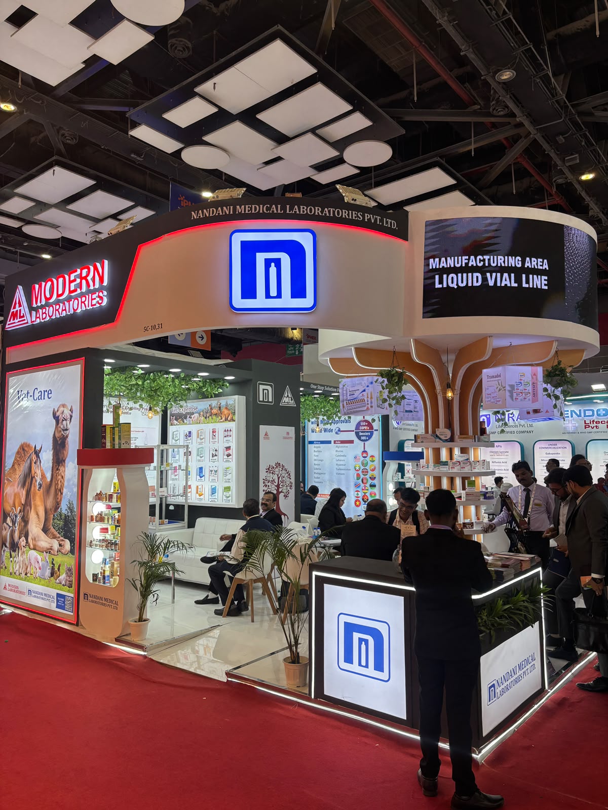 Nandani stall seen from the front-left corner — Modern Laboratories arch, illuminated ML monogram and red-carpet aisle